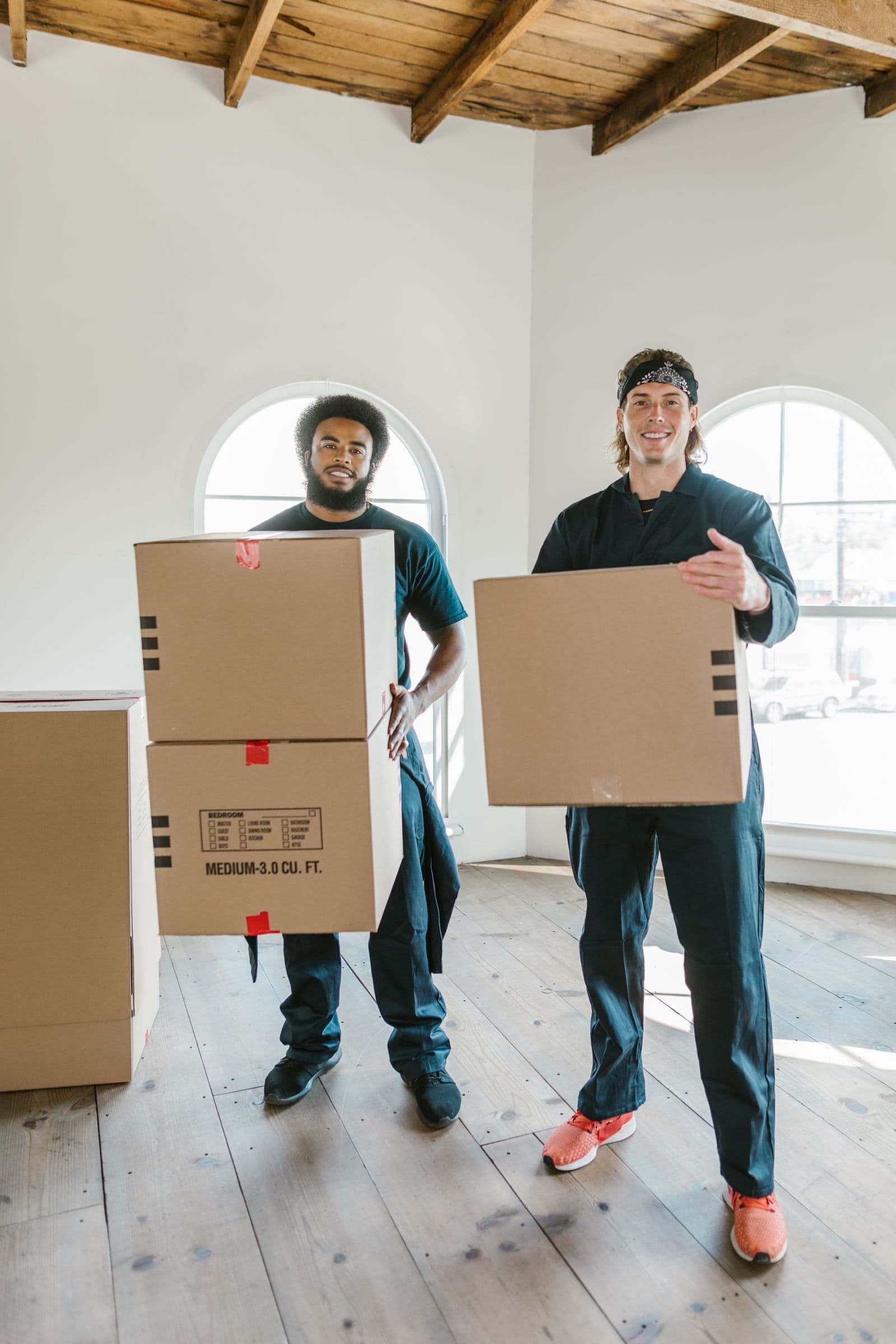 Two movers carrying cardboard boxes through a bright room